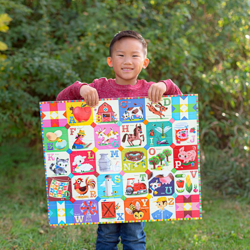 Child holding a colorful alphabet puzzle outdoors with greenery in the background